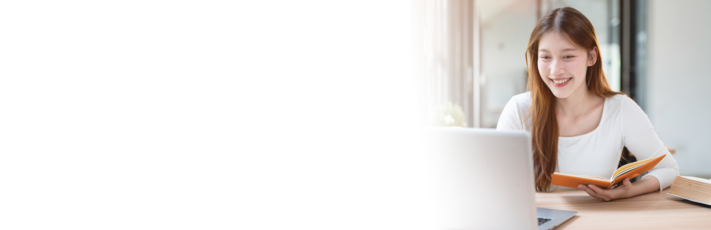 Young woman smiling while holding a book and looking at her laptop