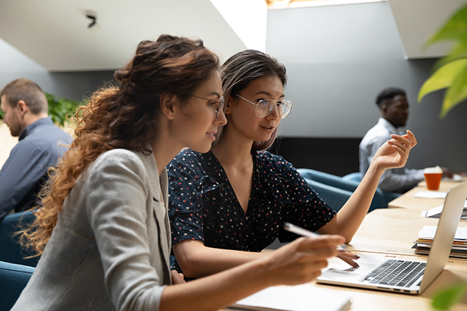 Two young women working together in front of a laptop